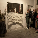 Twee vrouwen onthullen een kunstwerk aan de muur ten overstaan van geïnteresseerd publiek